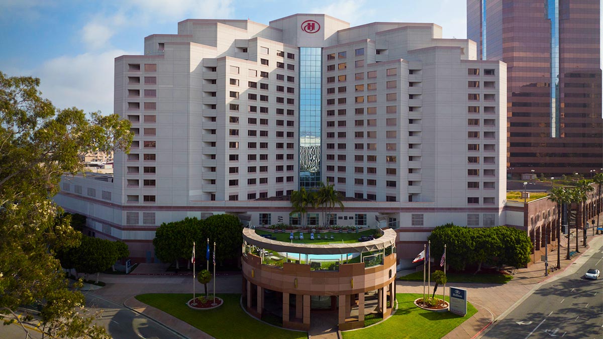aerial of exterior of Hilton Long Beach Hotel with view of street and building in the background during day with blue sky and clouds in Los Angeles, California, USA